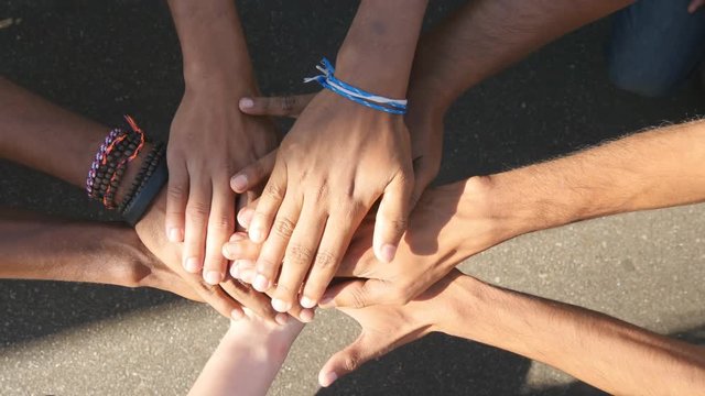 Arm of all races and colors stacked together one by one in unity and teamwork and then raised. Many multiracial hands getting together in the center of a circle and then cheer. Close up outdoor shot