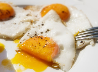 Three fried eggs for breakfast on a white  plate, one is half-cut, close-up