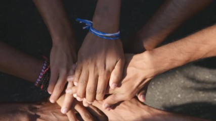 Arm of all races and colors stacked together one by one in unity and teamwork and then raised. Many multiracial hands getting together in the center of a circle and then cheer. Close up outdoor shot