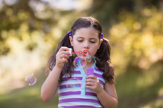 Girl blowing bubbles with wand on sunny day in forest