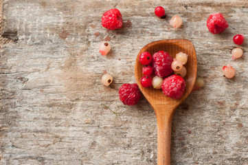 Fresh frozen raspberries and currant on wooden spoon isolated on wooden background