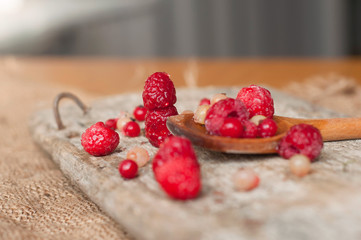 Fresh frozen raspberries and currant on wooden spoon isolated on wooden background