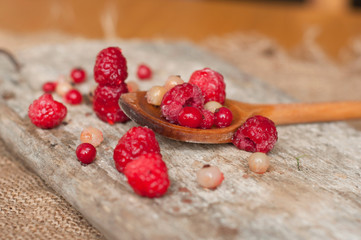 Fresh frozen raspberries and currant on wooden spoon isolated on wooden background