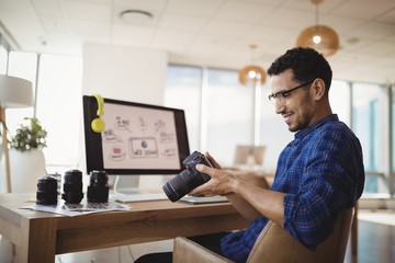 Smiling graphic designer looking at digital camera at desk