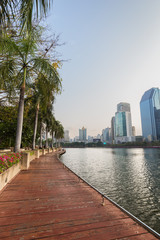 Fototapeta na wymiar View of palm trees, Wooden boardwalk and lake at the Benjakiti (Benjakitti) Park and modern skyscrapers in Bangkok, Thailand.