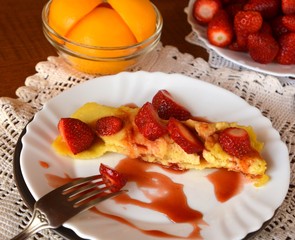Sweet homemade pancakes with syrup and strawberries decorated on a white plate.