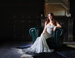 beautiful woman in evening dress sitting on a leather armchair in a luxurious interior