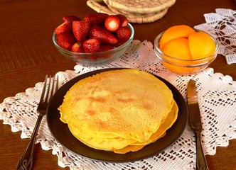 Stack of sweet pancakes decorated on a plate on a wooden table.