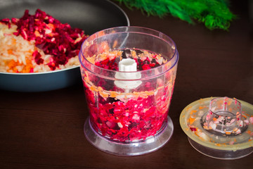Carrots, beets and onions are cut for frying for borsch in an electric chopper. Soup cooking.