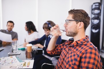 Businessman drinking water while sitting with colleagues