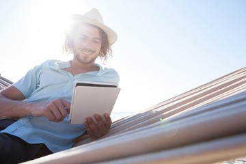 Man relaxing on hammock and using digital tablet on the beach