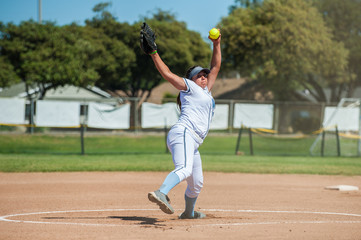 White uniform fast pitch softball pitcher winding up to throw in front view. 