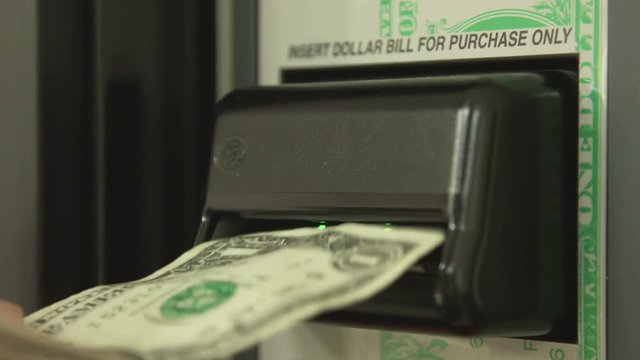 Close up of a man's hand feeding a one dollar bill into an automated vending machine. Shot in 4K UHD.