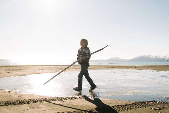 Boy walking with long stick on beach