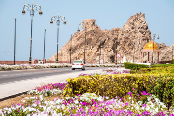 Ulica wzdłuż wybrzeża w Muscat z widokiem na ruiny fortu na skale.  - obrazy, fototapety, plakaty