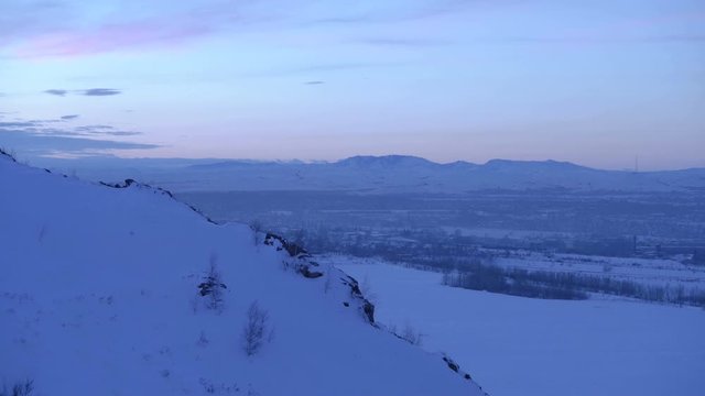 Time lapse of industrial city surrounded by mountains at dusk in winter.