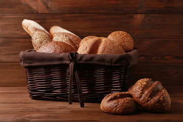 Wicker basket with different types of fresh bread on wooden table