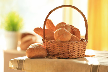 Wicker basket with different types of fresh bread on table
