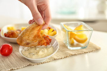 Hand of woman eating chicken wings with tasty mayonnaise sauce, closeup