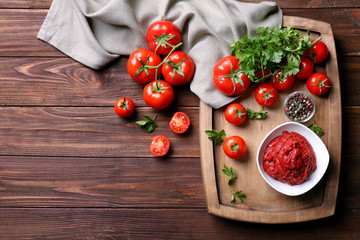 Delicious tomato paste in bowl with ingredients on wooden background, top view