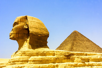 Close up of the face of the Great Sphinx with a set of pyramids in the background on a beautiful clear blue sky day in Giza, Cairo, Egypt  © Thomas Sztanek