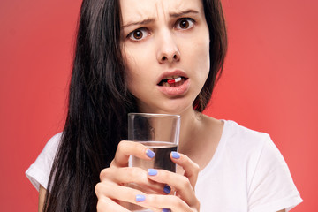 woman with a glass of water and a pill in her teeth, emotions, medicines, red background