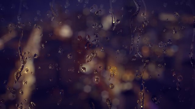 Background shot of rainy water drips on a window glass. A nighttime city scene with traffic is defocused in the distance.  	