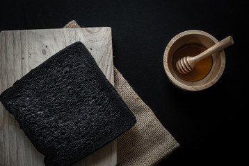 Black charcoal sliced bread with honey on rustic wooden cutting board over black backdrop, top view, Healthy eating concept.