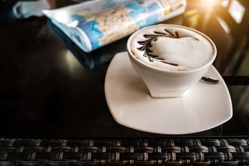 Cup of  hot mocha with newspaper/map on the table, coffee shop background, warm and dark tone, selective focus.