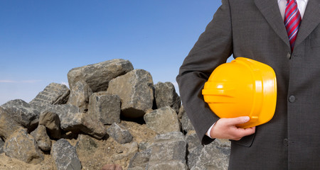 Ingenieur im Anzug mit gelbem Helm vor einer Baustelle