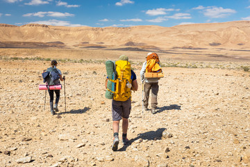 Fototapeta na wymiar Three backpackers walking stone desert trail.