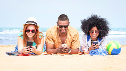 Row of multicultural friends using phone lying on beach - Happy african and american students on...