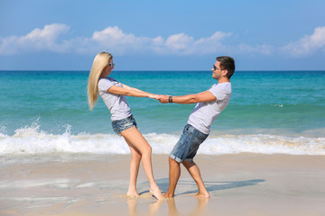 Young happy couple on beach smiling holding hands around each other. Love story