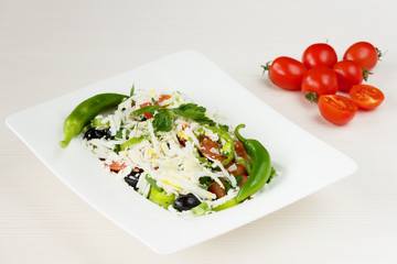 Traditional classic Shopska salad with tomatoes, peppers, cucumbers and cheese in white dish on white wooden table. Bulgarian cuisine, Balkan culture