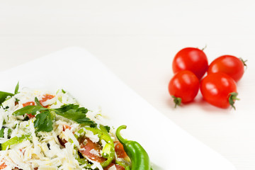 Traditional classic Shopska salad with tomatoes, peppers, cucumbers and cheese in white dish on white wooden table. Bulgarian cuisine, Balkan culture