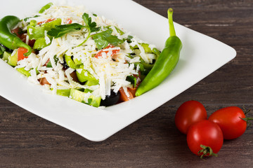 Traditional classic Shopska salad with tomatoes, peppers, cucumbers and cheese in white dish on grey wooden table. Bulgarian cuisine, Balkan culture