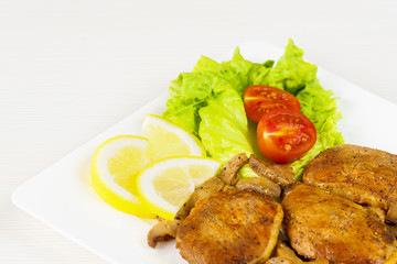 Pork fillet steak with cherry tomatoes, lemon and a lettuce in white dish on white background