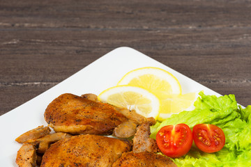 Pork fillet steak with cherry tomatoes, lemon and a lettuce in white dish on grey background.