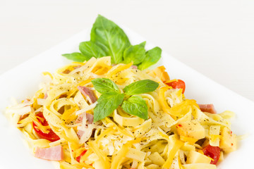 Tagliatelle pasta with pesto sauce, bacon, Gauda, Cheddar, Emmental cheese and basil leaves in white plate on white wooden background. Close up image - healthy homemade pasta