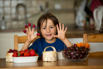 Cute sweet child, boy, eating fresh fruits at home, strawberries, cherries, raspberries, blueberries