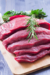 Fresh raw beef steak with rosemary on a wooden table. Dark background.