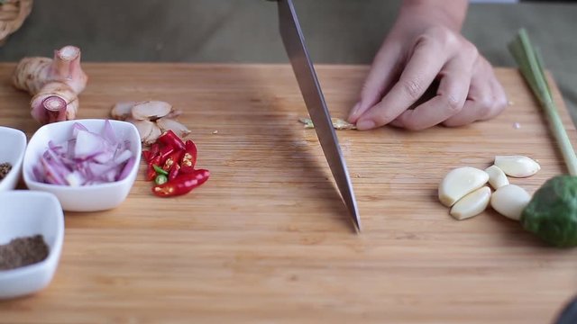 A female hand cut coriander root and crack it on bamboo wooden plate with other Thai herbs beside for Tom Yum recipe.