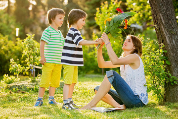 Young beautiful mother, sitting in a garden, little boys, her sons, bringing gerbera flowers and present © Tomsickova