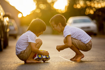 Two sweet children, boy brothers, playing with car toys on the street in village on sunset