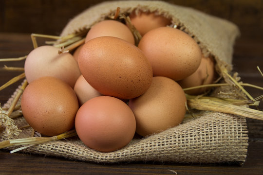 Chicken eggs with straw in bag on wooden background