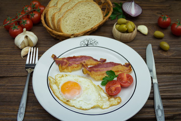 Fried eggs and bacon in a plate for breakfast on a wooden background