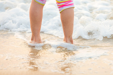 Children's legs stand on the beach.