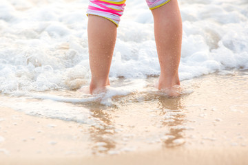 Children's legs stand on the beach.