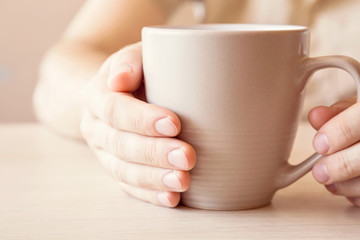 Man drinking morning coffee at the table in the kitchen. Hands holding a mug.