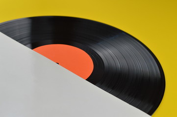 old black vinyl record with blank orange label halfway out of its white blank cover on yellow...